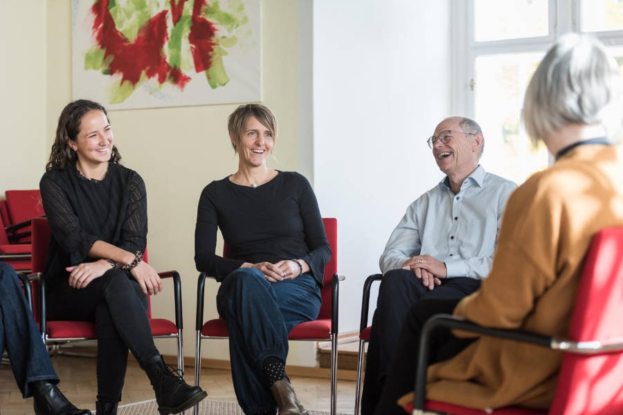 Mehrere Personen sitzen in einem Stuhlkreis und lachen oder lächeln
