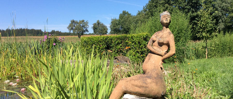 Skulptur einer nackten Frau, umgeben von Natur, an einem See © Robin Menges