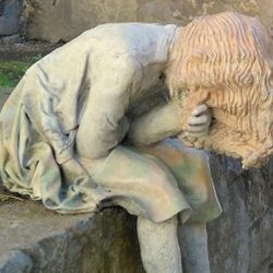Steinfigur: ein Mädchen sitzt vornübergebeugt auf einer Mauer und hält sich eine Hand ins Gesicht. Die langen Haare verdecken das Gesicht. Oslo. © Robin Menges